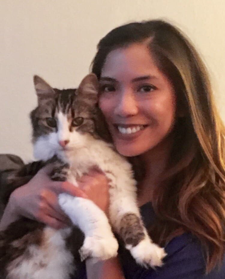 Woman smiling holding up her long-haired white, brown and black cat.